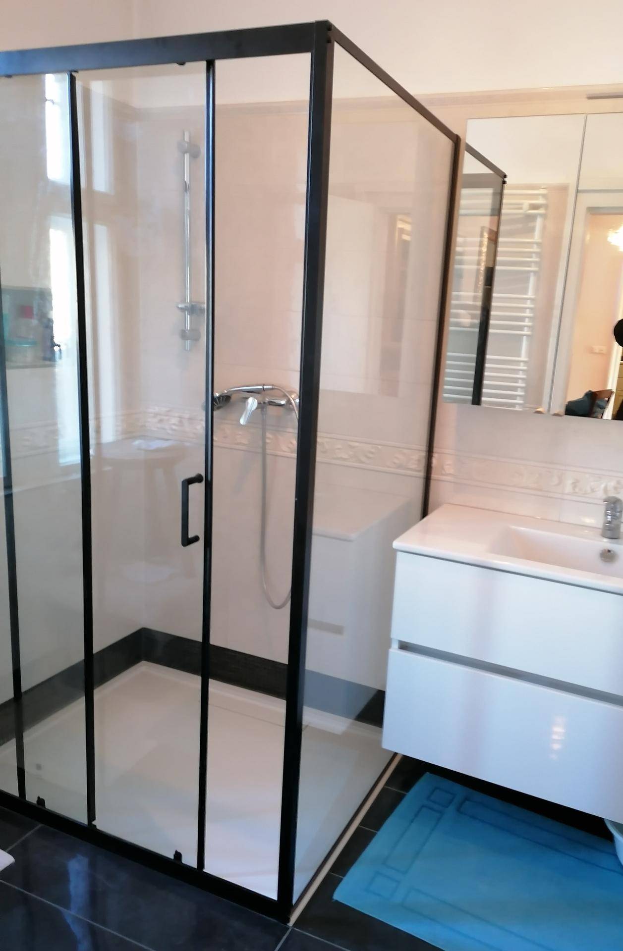 Modernes Badezimmer mit Duschkabine, weißem Waschtisch und beheiztem Handtuchhalter.