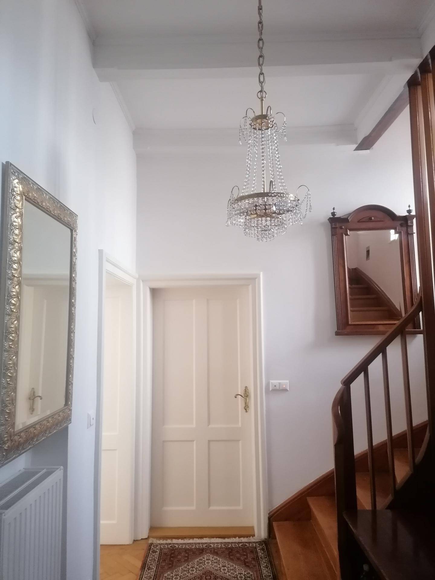 Heller Flur mit Holztreppe, Kronleuchter und dekorativen Spiegeln.