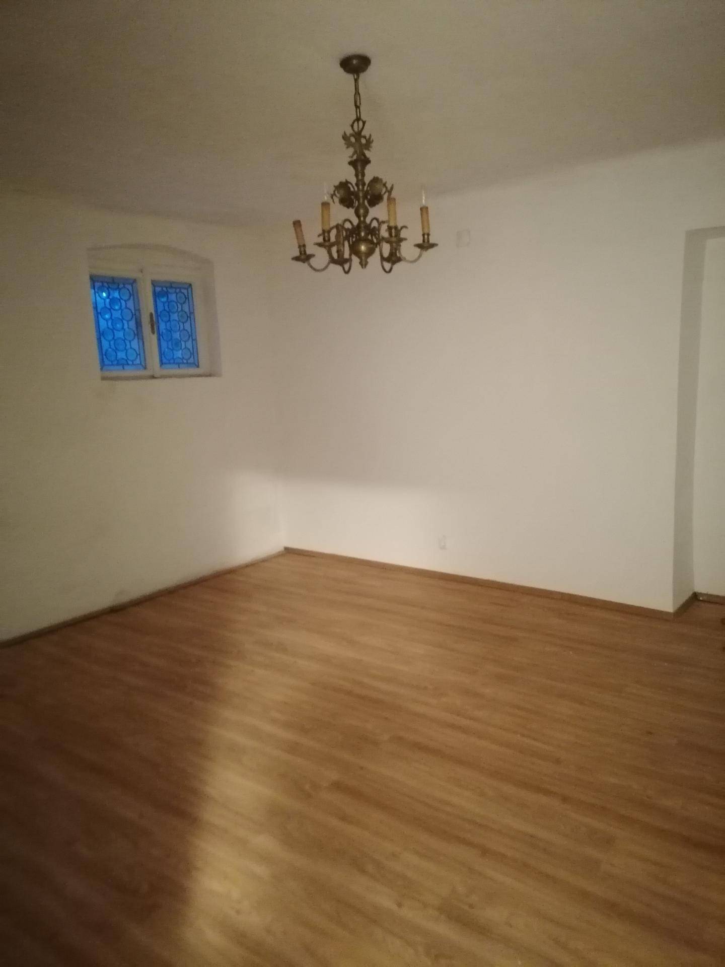 Leerer Raum mit Holzboden, einem Kronleuchter und einem kleinen Fenster.