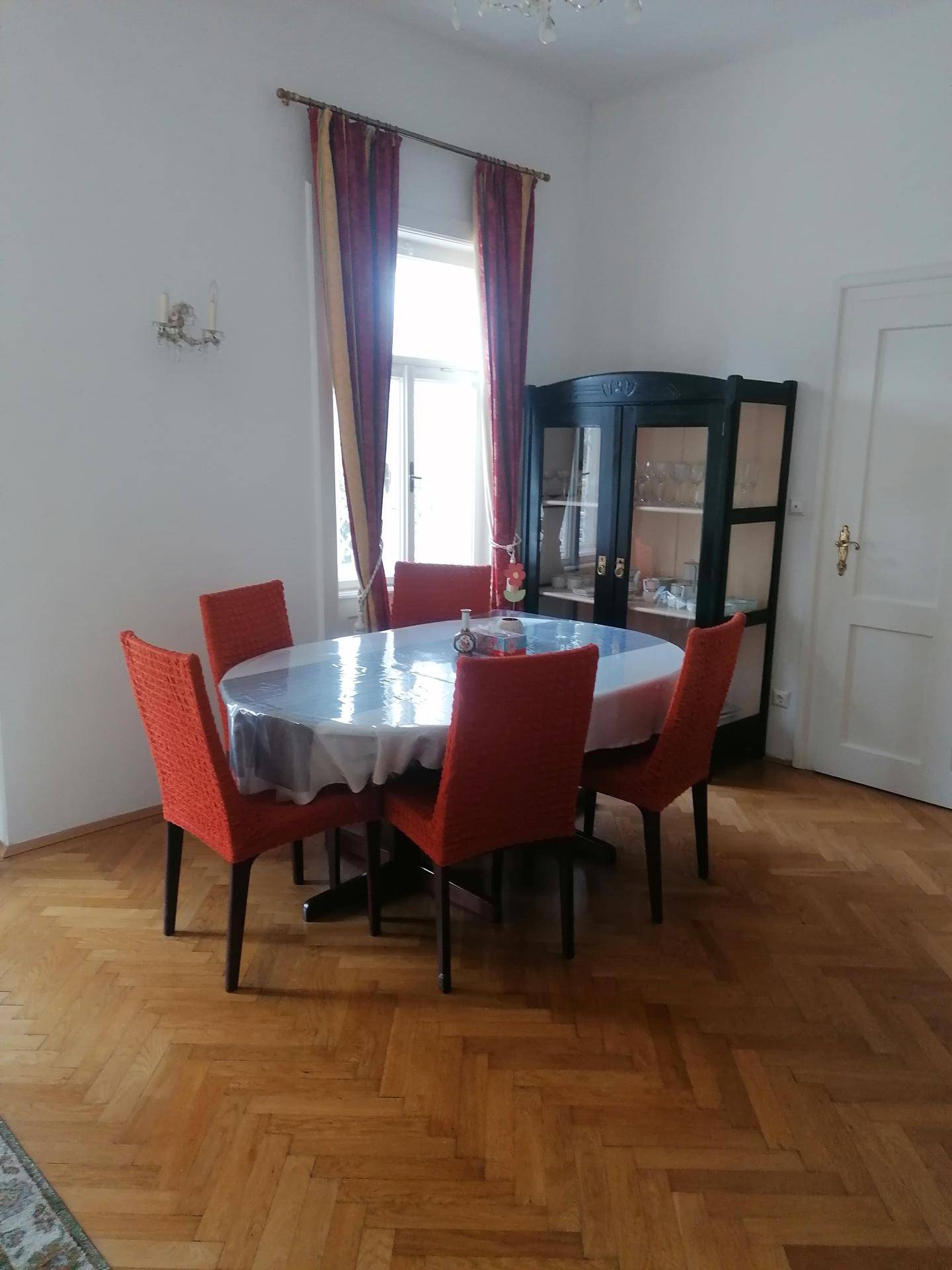 Heller Essbereich mit Fischgrätparkett, rotem Mobiliar und einem Vitrinenschrank.