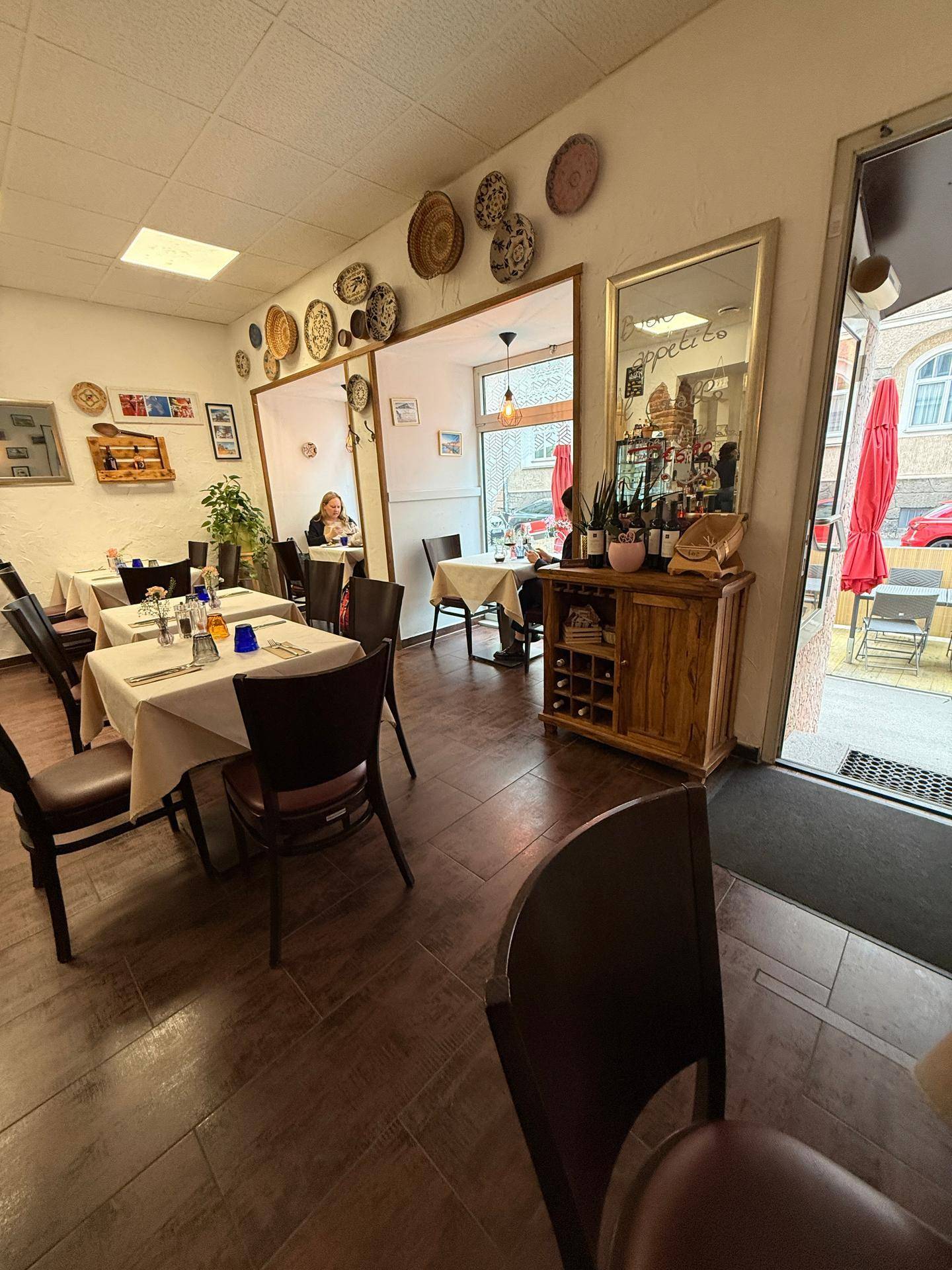 Heller Gastraum eines Restaurants mit mehreren Tischen, Holzmöbeln und einem Spiegel, der den Raum erweitert.