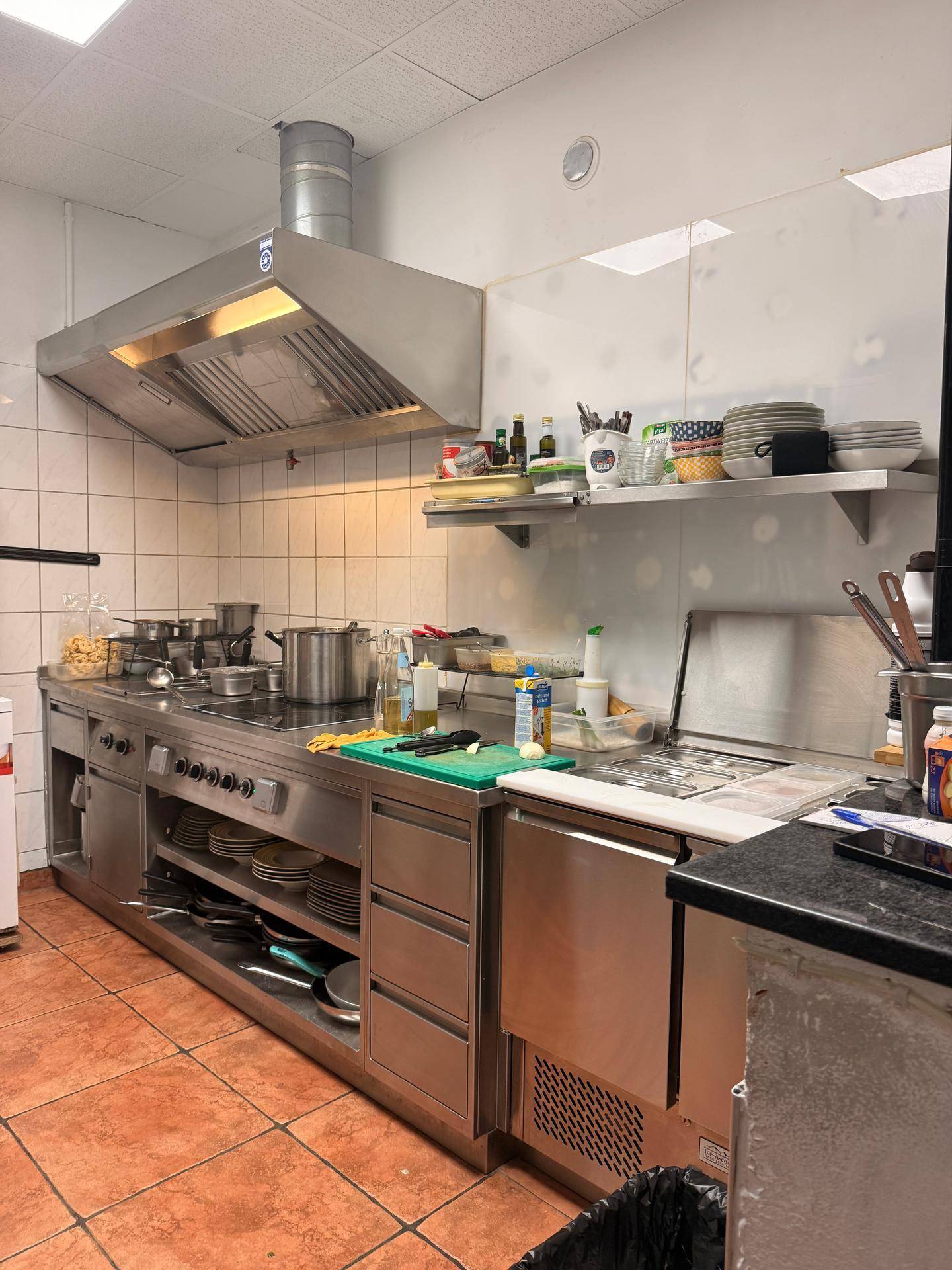 Professionelle Gastronomieküche mit großer Dunstabzugshaube, mehreren Kochfeldern und Arbeitsflächen.