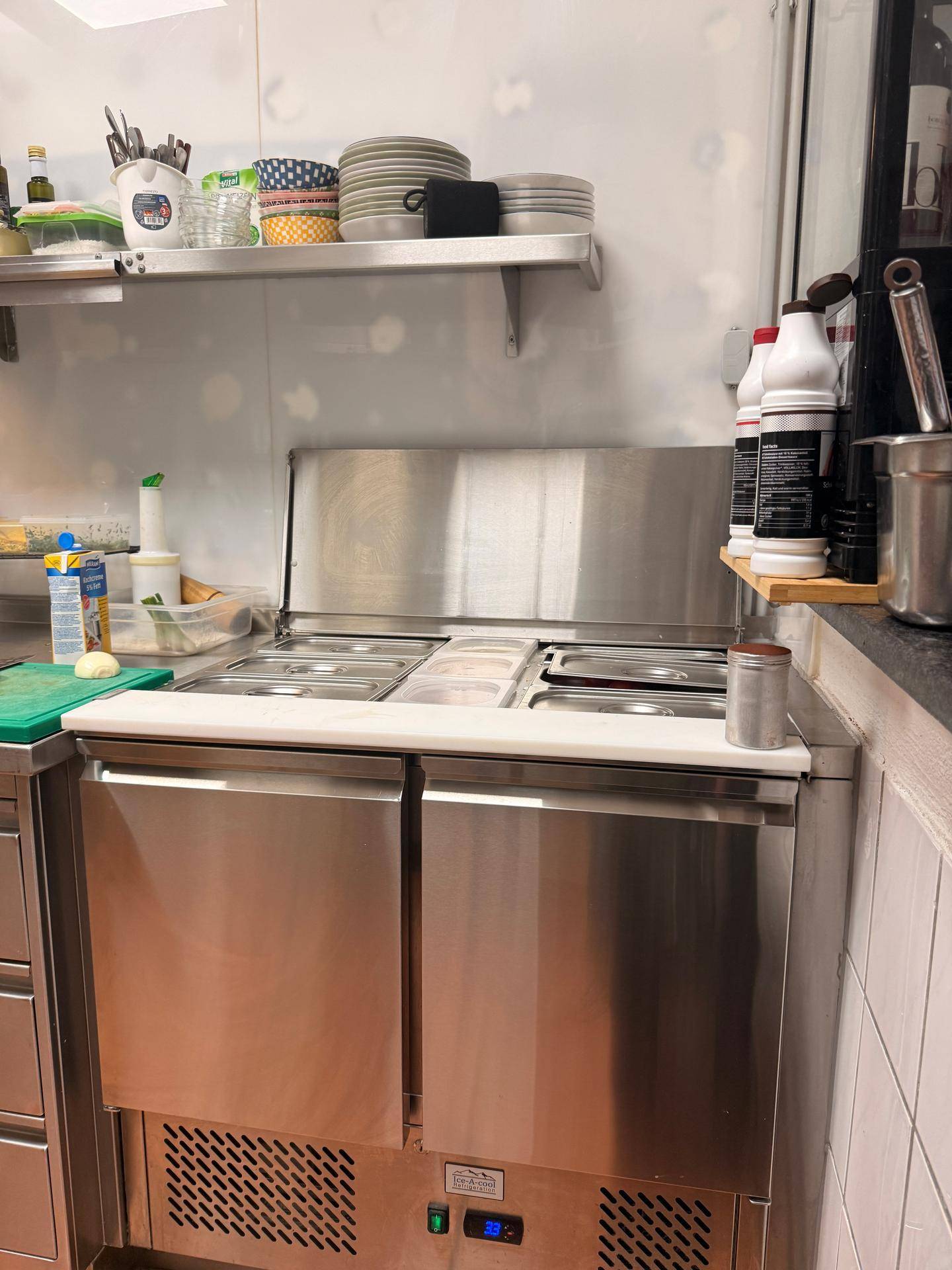Nahaufnahme einer gekühlten Vorbereitungsstation mit Edelstahloberflächen in einer professionellen Küche.