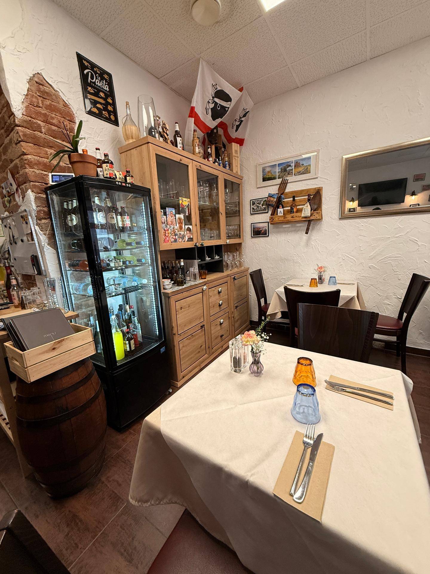 Gemütlicher Restaurant-Essbereich mit gedeckten Tischen, Holzmöbeln und einer beleuchteten Getränkevitrine.