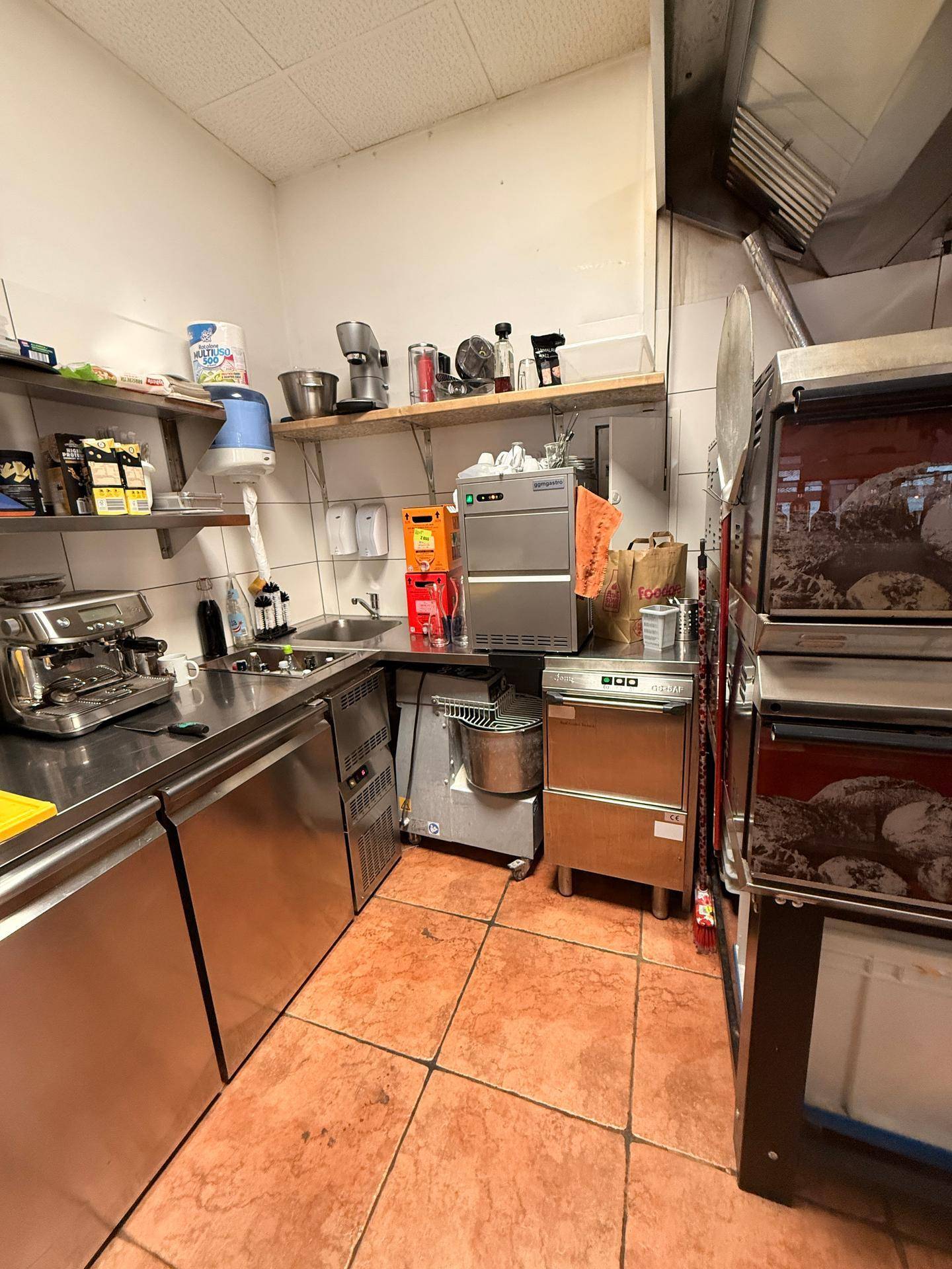 Professionelle Restaurantküche mit Edelstahleinrichtungen, Spülbecken und Regalen für Küchenutensilien.