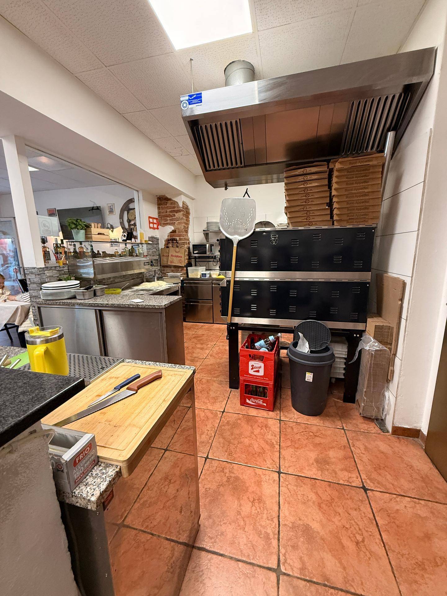 Große gewerbliche Küche mit Dunstabzugshaube, Pizzaöfen und einem Arbeitsbereich mit Schneidebrett.