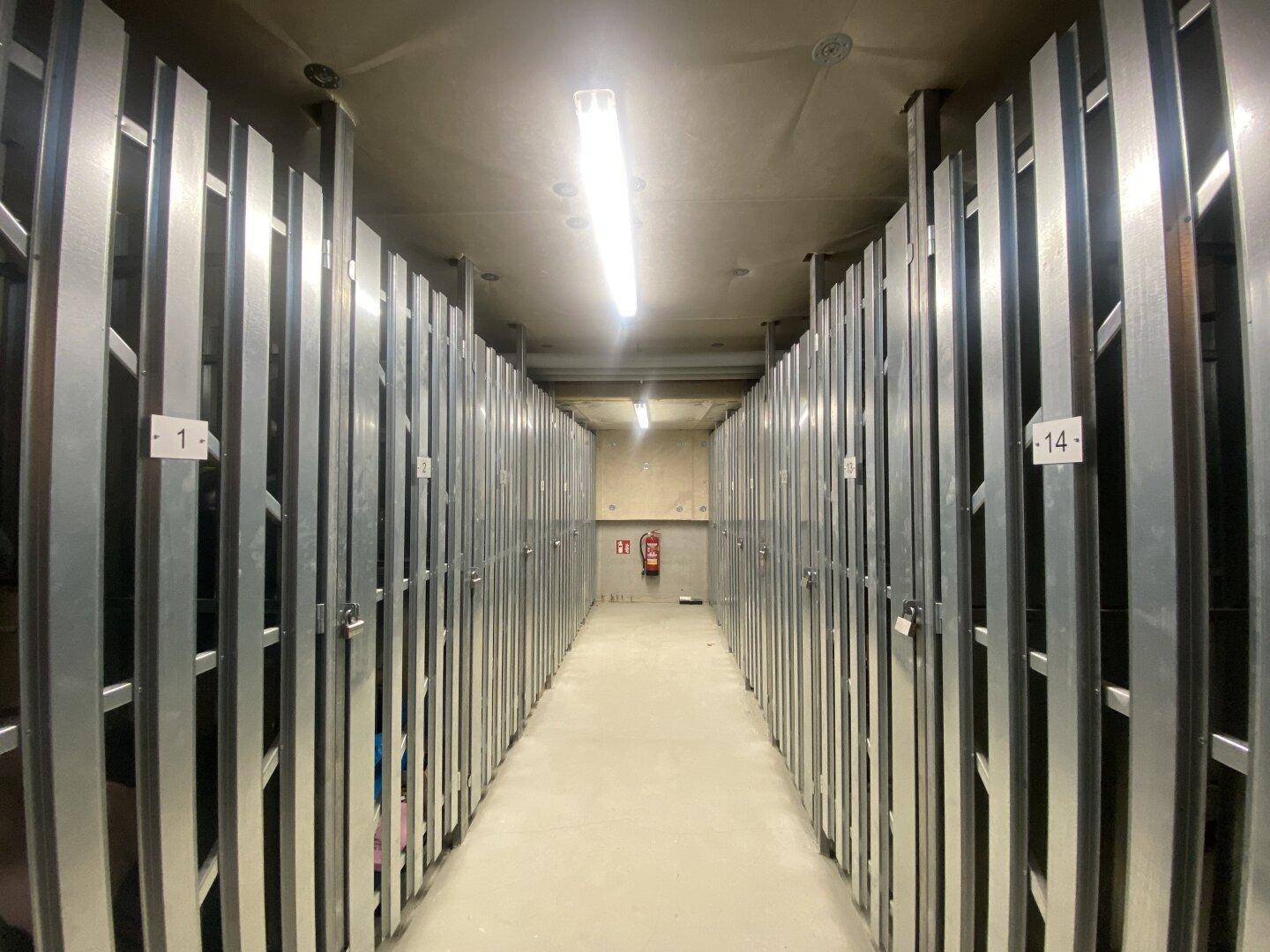 Gemeinschaftlicher Kellerbereich mit individuellen Abstellabteilen und funktionaler Beleuchtung.