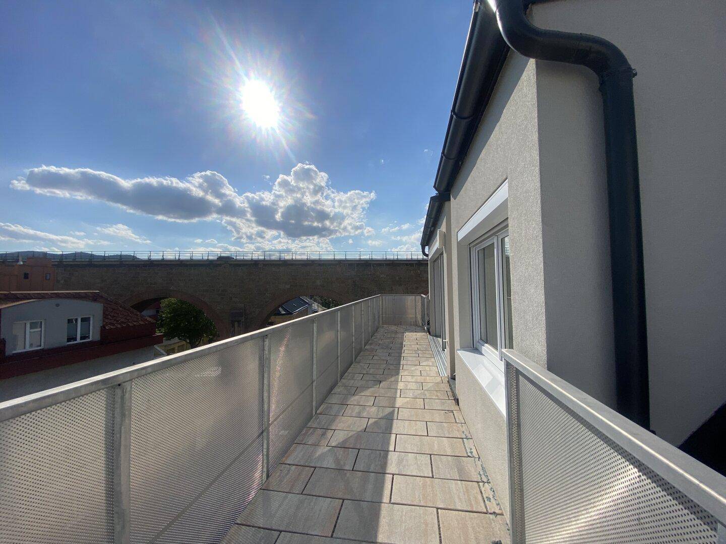 Sonniger Terrassenbereich mit Fliesenboden und Blick auf eine historische Brückenkonstruktion.