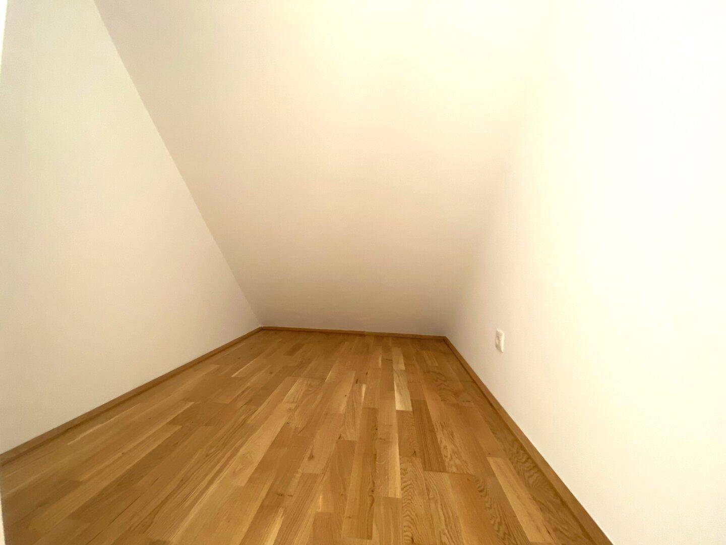 Kleiner Raum mit Holzboden und Dachschräge, ideal als Abstellraum oder kleines Büro.