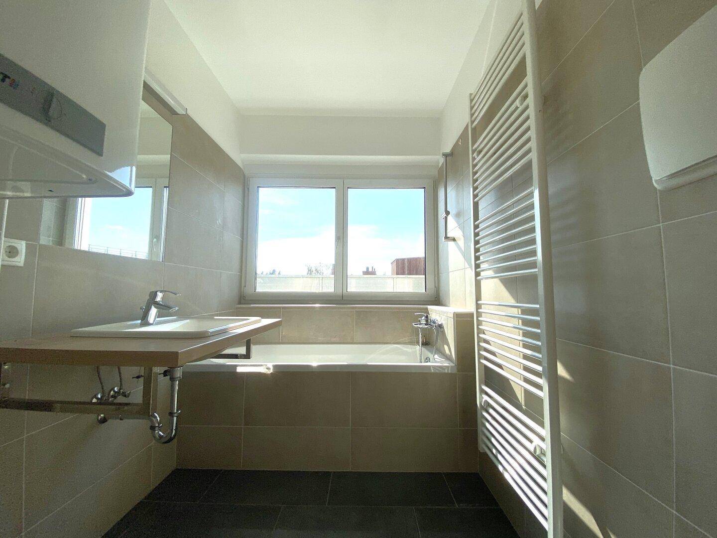 Modernes Badezimmer mit beigefarbenen Fliesen, Badewanne, Einzelwaschbecken und Fenster.