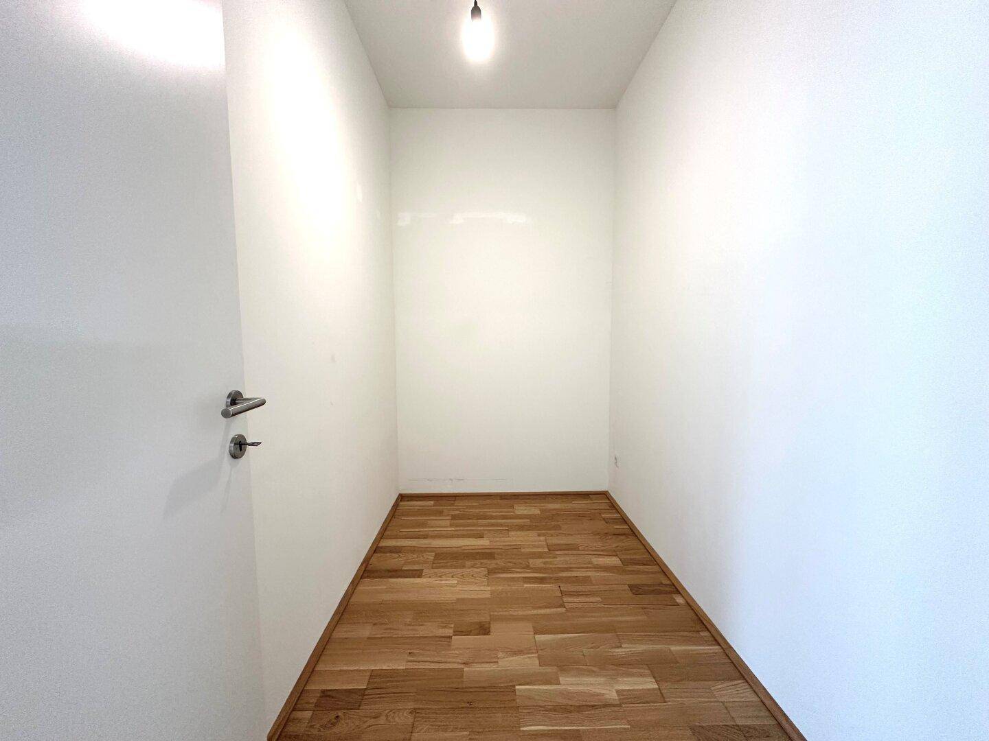 Kleiner, leerer Raum mit Holzfußboden und weißen Wänden, ideal als Abstellraum oder begehbarer Kleiderschrank.