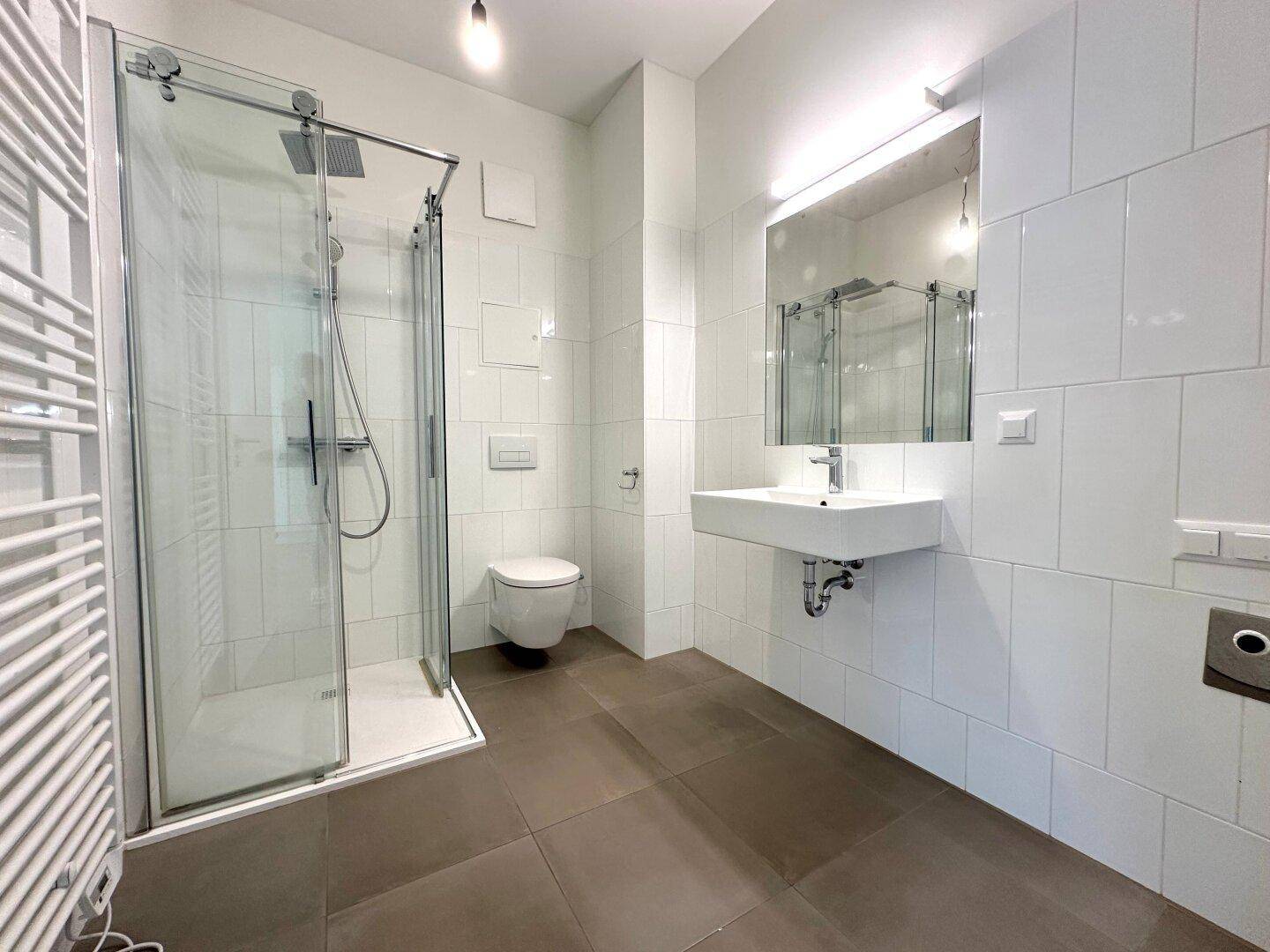 Modernes Badezimmer mit weiß gefliesten Wänden, dunklem Boden, ebenerdiger Dusche und Wand-WC.