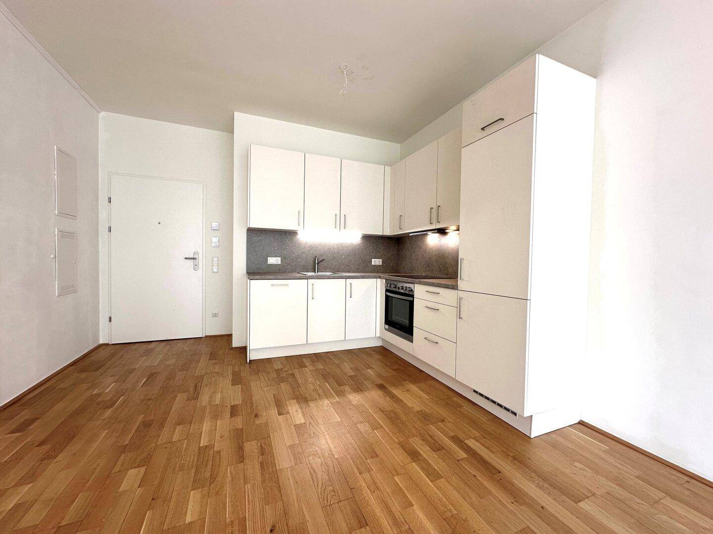 Moderne Küchenzeile mit weißen Schränken und integriertem Backofen in einem leeren Raum mit Holzfußboden.
