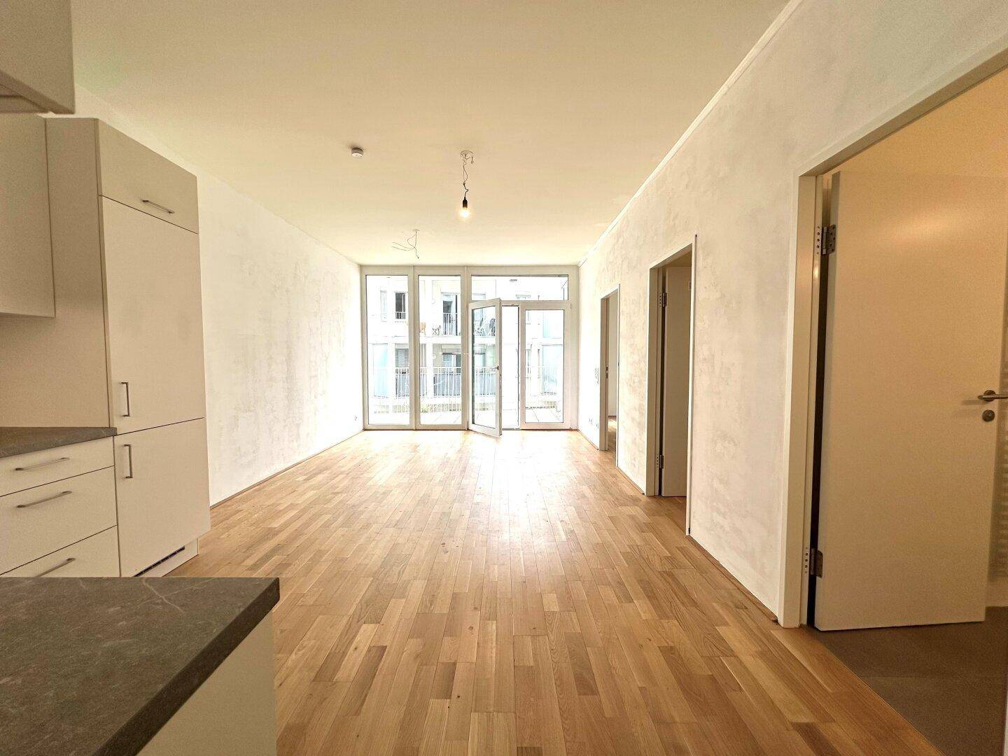 Heller, leerer Wohnbereich mit Eichenparkett und großen Fenstertüren, die viel Tageslicht hereinlassen.