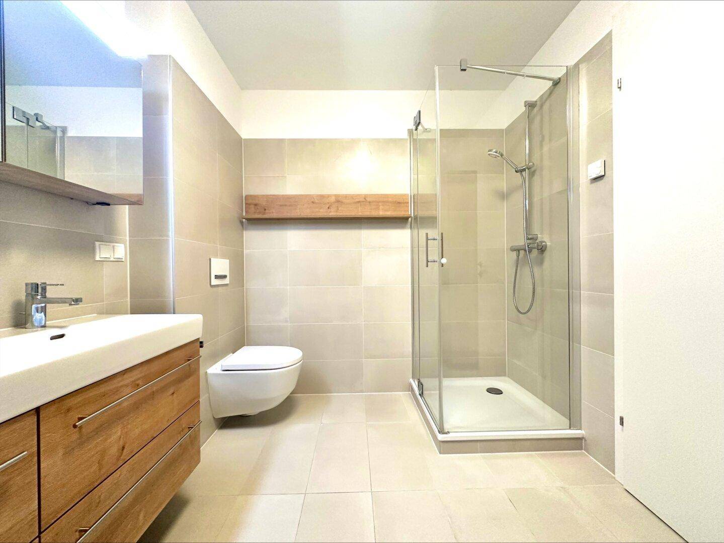 Elegantes Badezimmer mit ebenerdiger Dusche, wandhängendem WC und modernem Waschtisch, hell gefliest.