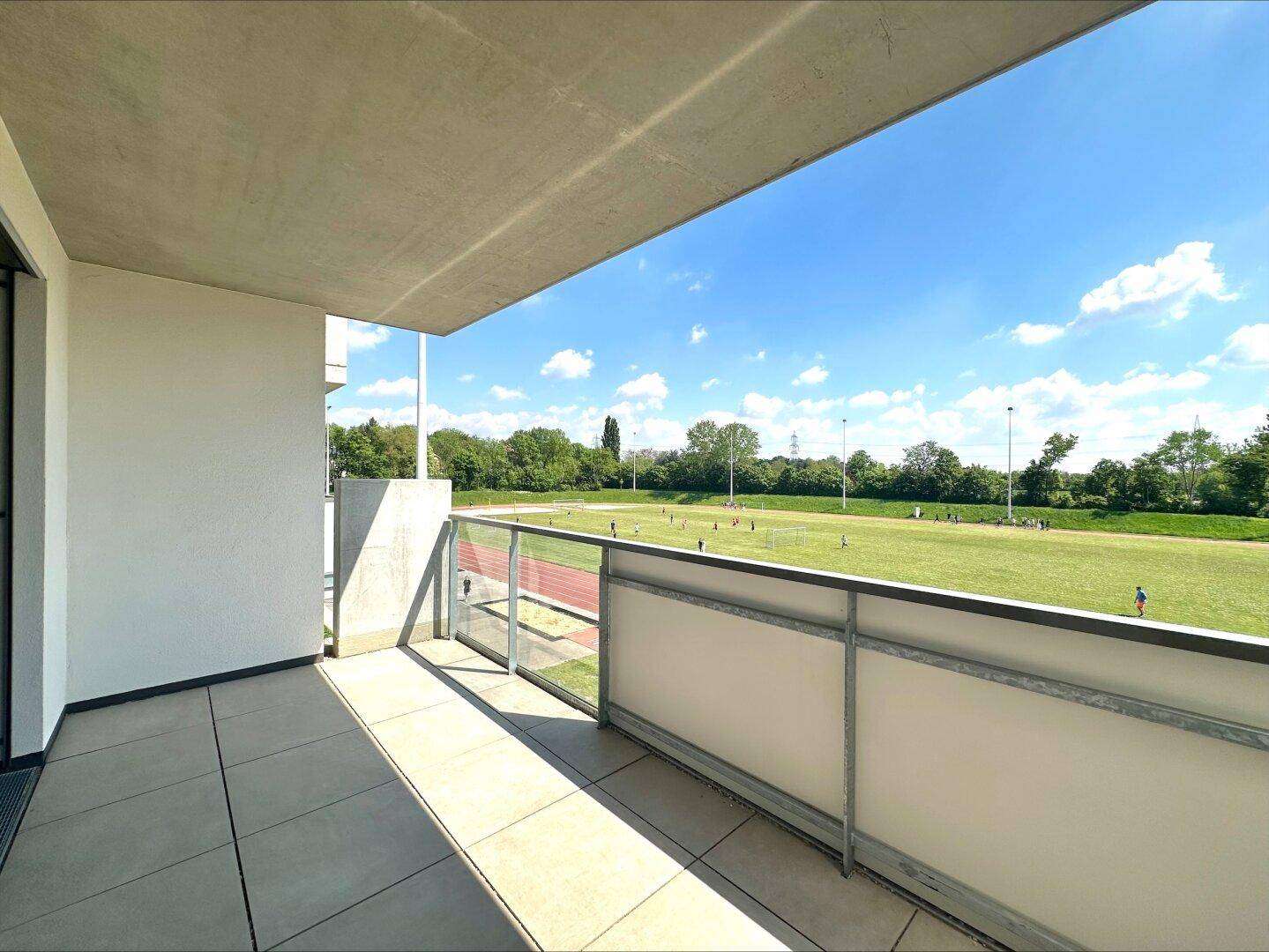 Geräumiger Balkon mit Blick auf ein Sportfeld, bietet viel Sonne und Platz für Entspannung.