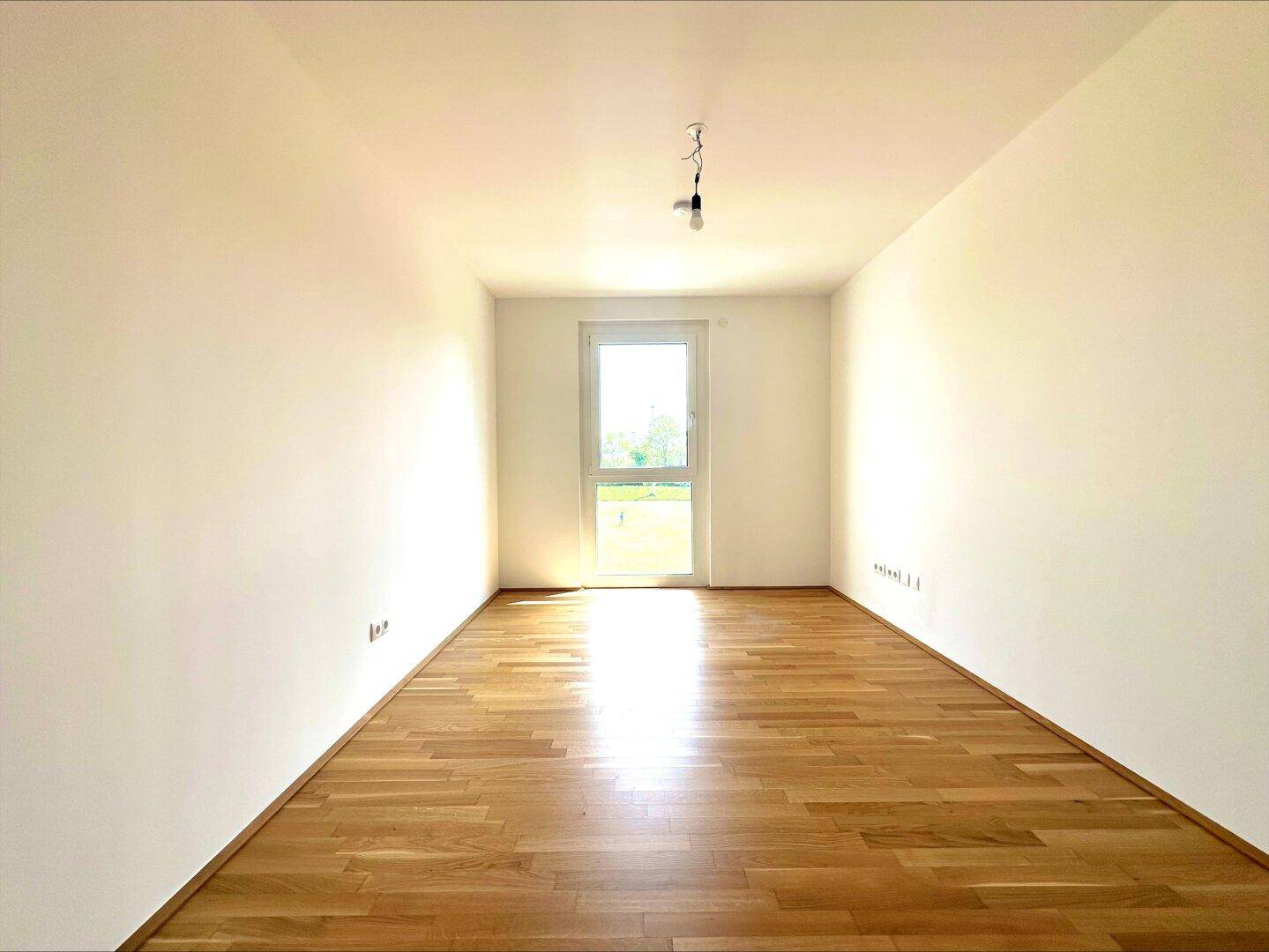 Lichtdurchflutetes Zimmer mit Parkettboden und direktem Zugang zum Außenbereich, bietet viel Helligkeit.