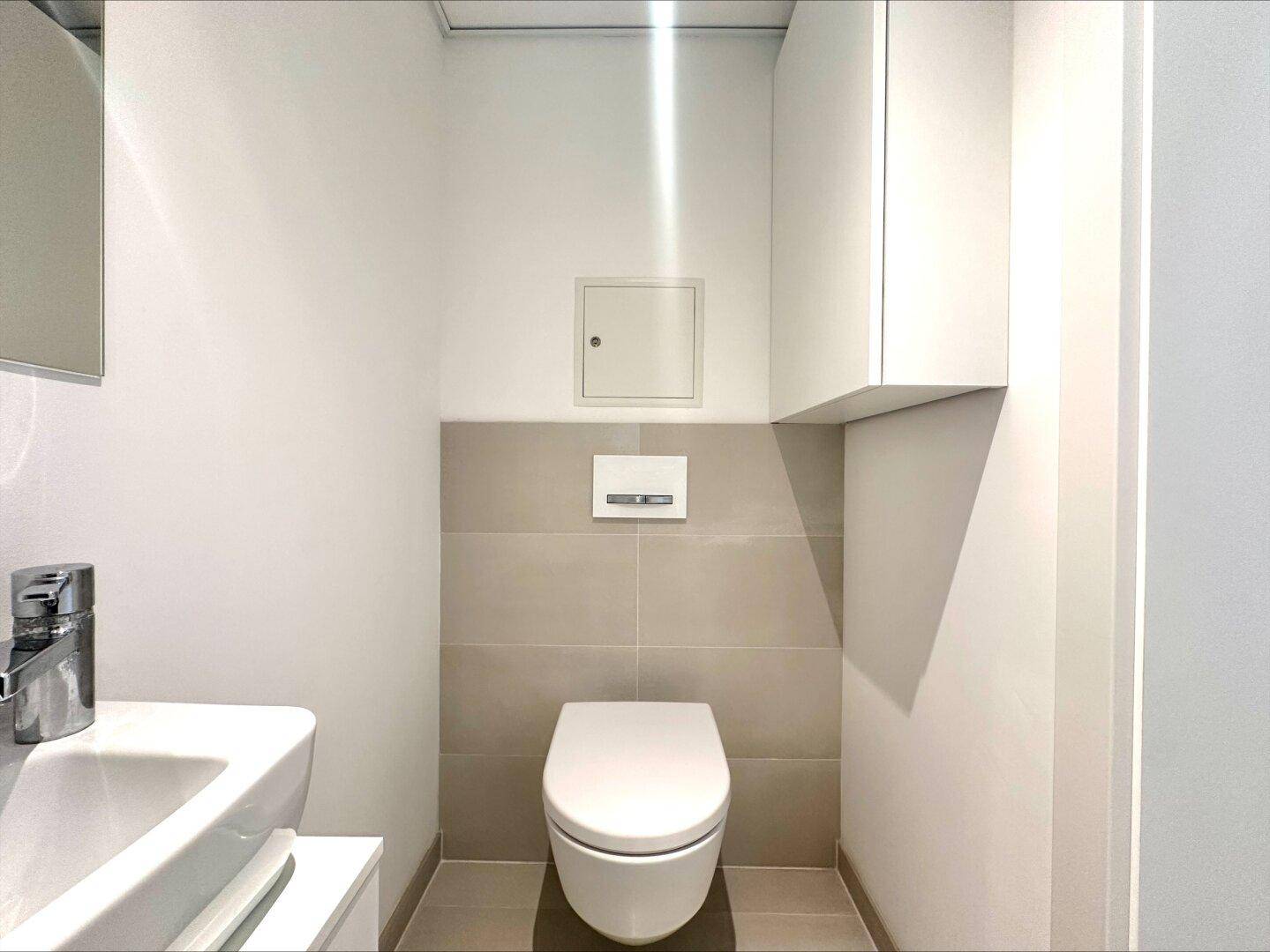 Separates Gäste-WC mit modernem wandhängendem WC und kleinem Waschbecken, in neutralen Farben gehalten.