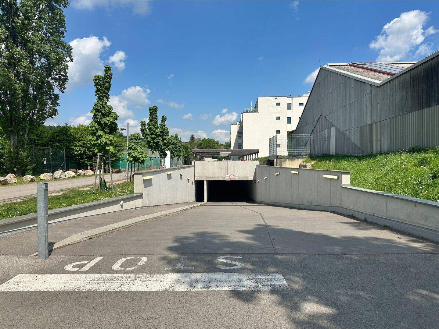 Zufahrt zur Tiefgarage eines modernen Wohnkomplexes, umgeben von Grünflächen und Bäumen.