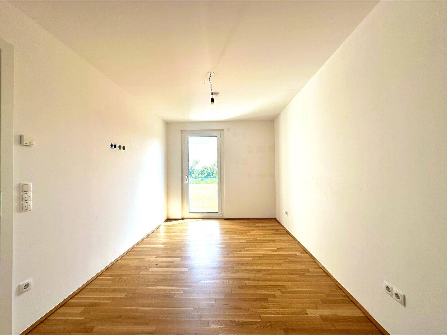 Geräumiges Zimmer mit hellem Parkettboden und Fenster zum Garten, bietet eine ruhige Wohnatmosphäre.