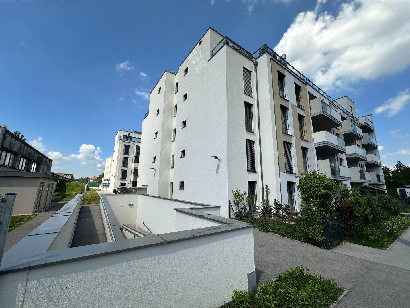 Moderne Wohngebäude mit weißer Fassade und Balkonen, eingebettet in eine grüne Umgebung.