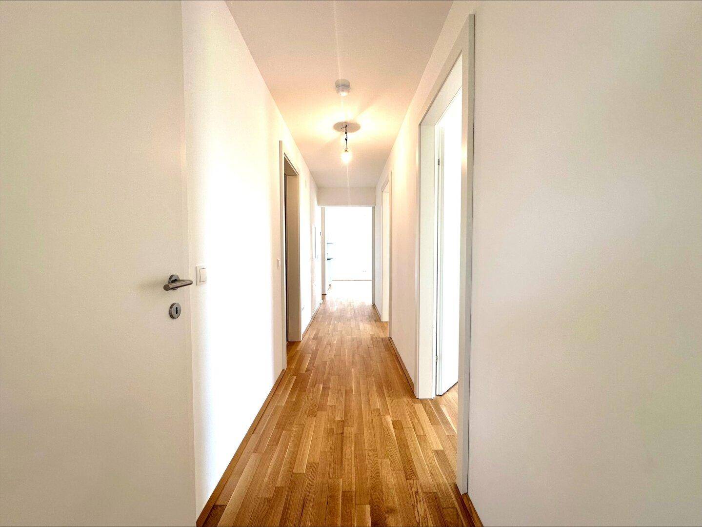 Langer, heller Flur mit Parkettboden, der zu den verschiedenen Zimmern der Wohnung führt.