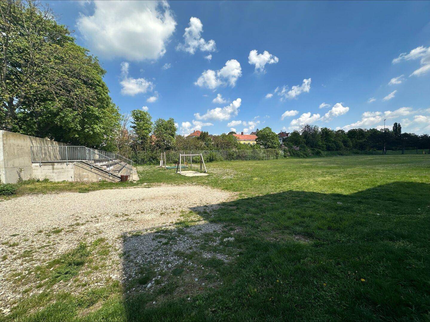 Große Grünfläche mit Spielgeräten und Tribüne, ideal für Sport und Freizeitaktivitäten im Freien.