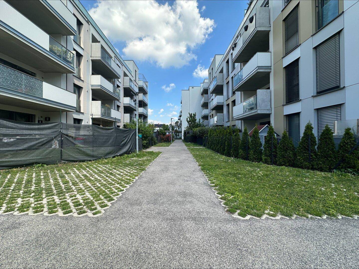 Fußweg zwischen modernen Wohngebäuden mit gepflegten Grünflächen und Hecken.