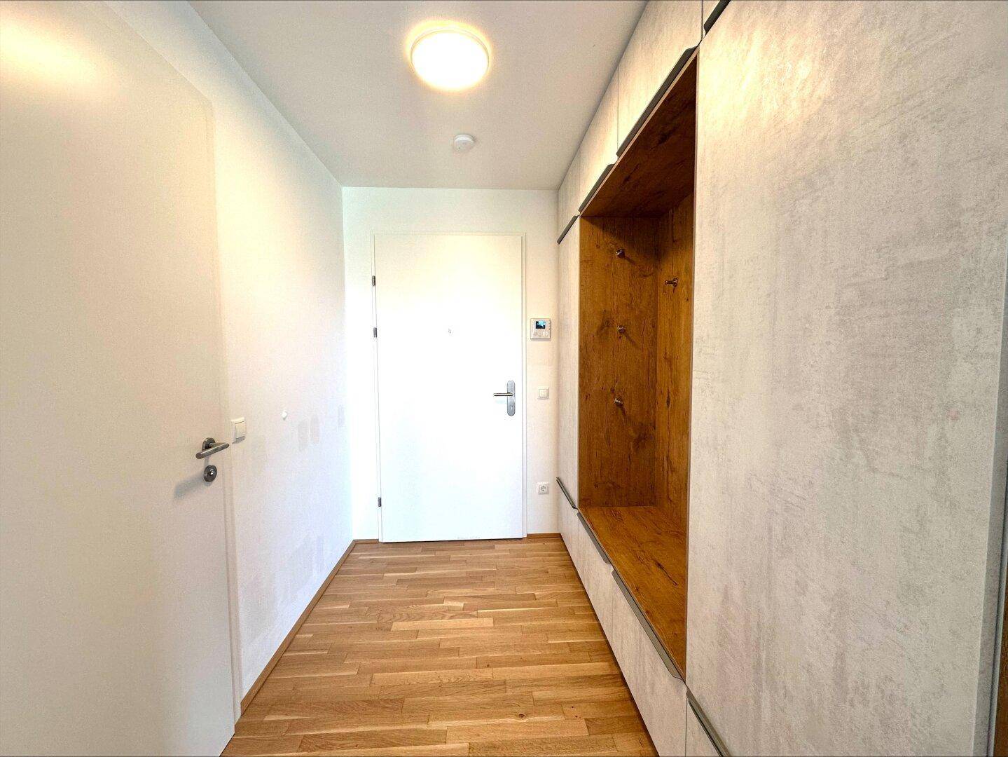 Heller Eingangsbereich mit Parkettboden und moderner Garderobe, führt zur Wohnungstür.