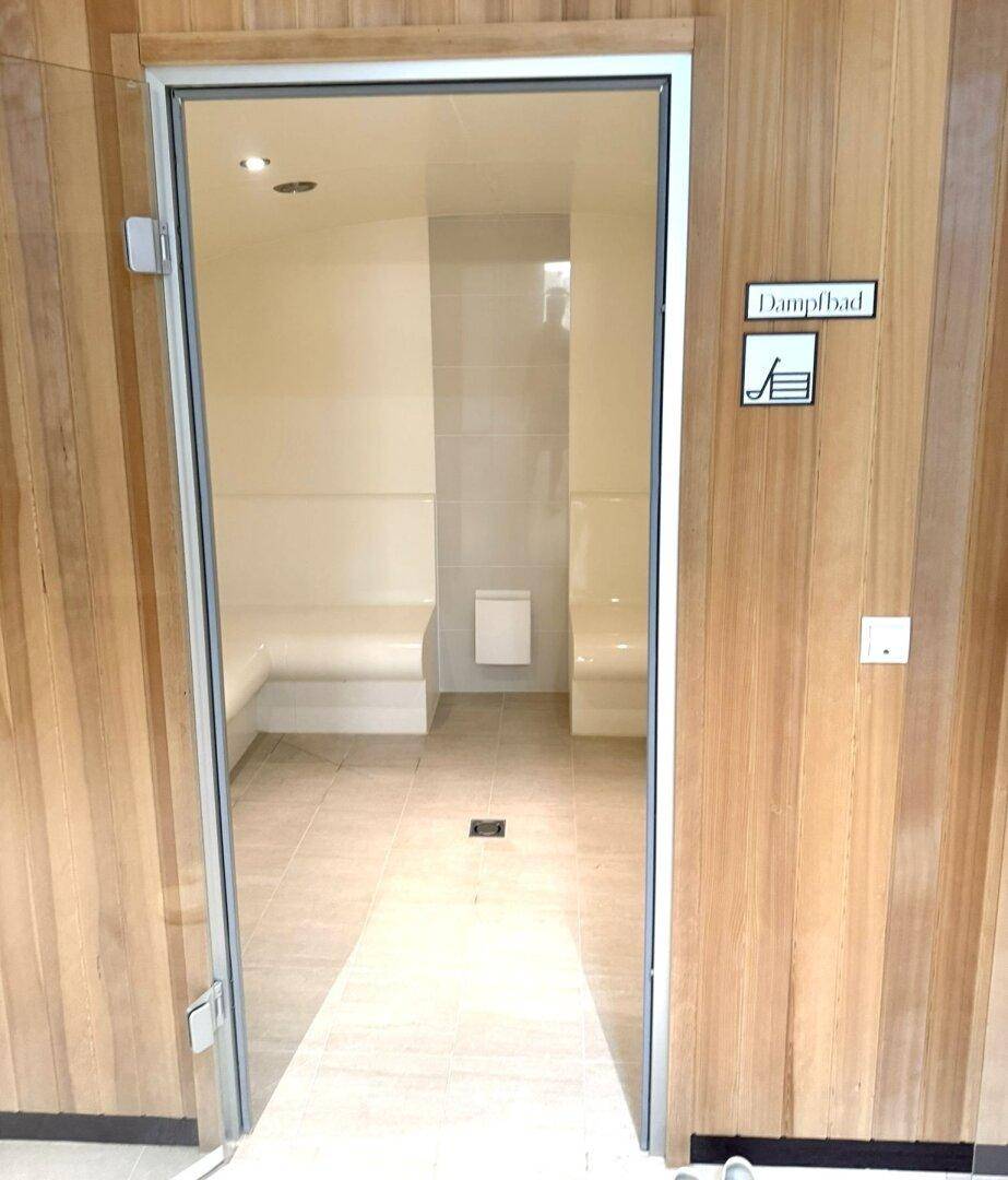 Modernes Dampfbad mit gefliesten Bänken und Glasfront, ideal zur Entspannung und Regeneration.