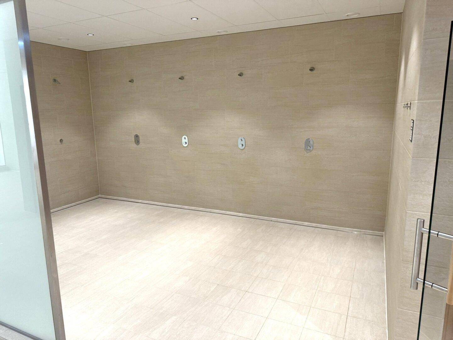 Geräumiger, leerer Raum mit hellen Fliesen, möglicherweise für Duschen oder Umkleiden im Wellnessbereich.