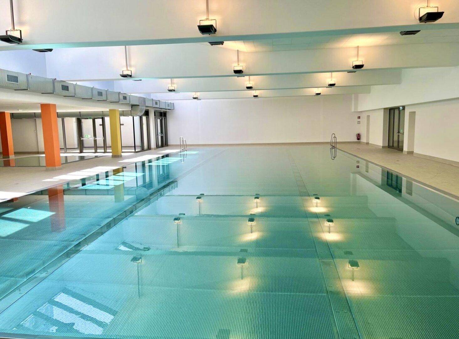 Großes Hallenbad mit hellblauen Fliesen und viel Tageslicht, ideal für sportliche Aktivitäten.