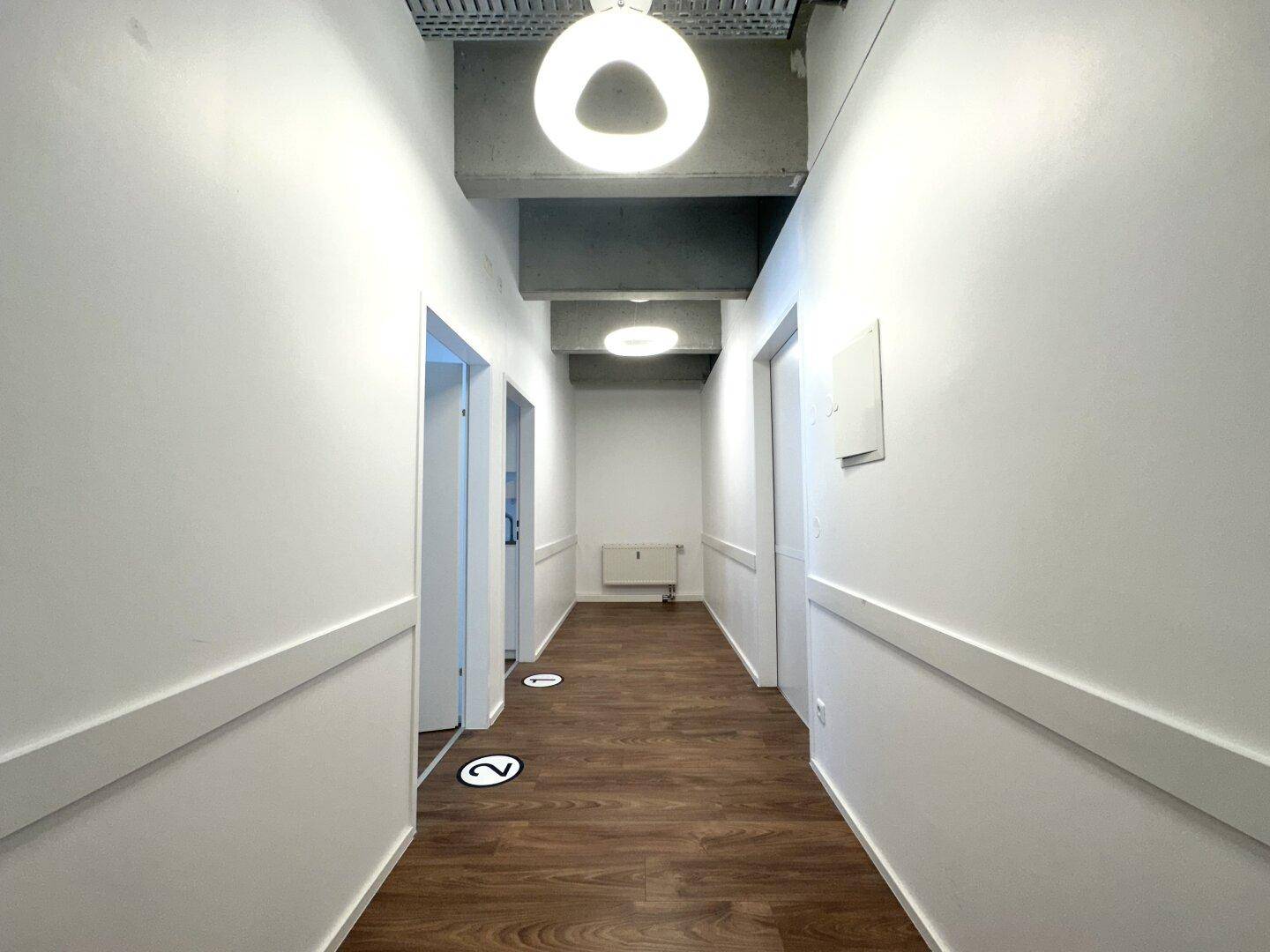 Heller Flur mit Holzboden und modernen runden Deckenleuchten, der zu verschiedenen Räumen führt.