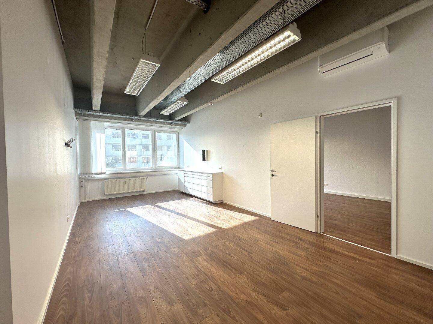 Geräumiges Büro mit Küchenzeile, großen Fenstern und Holzboden in einem modernen Gebäude.