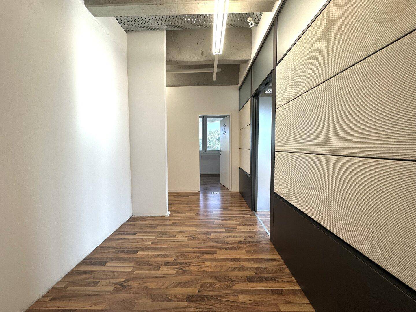 Modernes Büro mit Holzboden, weißen Wänden und einer stilvollen Trennwand mit Glaselementen.