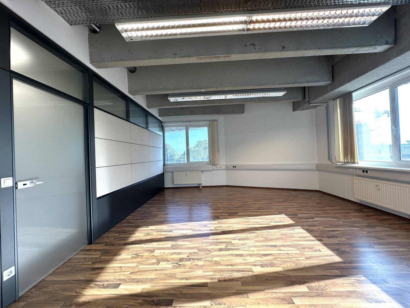 Helles Büro mit Holzboden, großen Fenstern und einer modernen Trennwand mit Glaselementen.