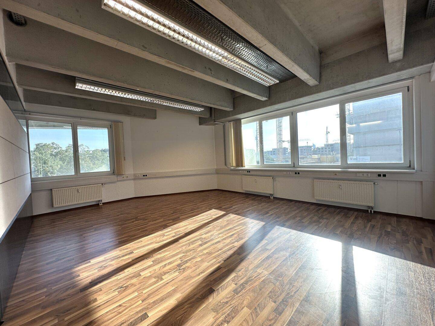 Großer, heller Büroraum mit Holzboden, weiten Fenstern und sichtbaren Deckenstrukturen.