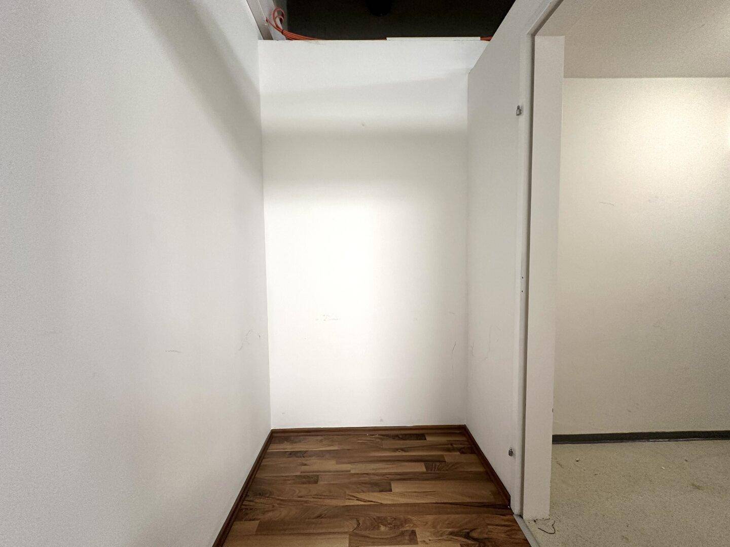 Kleiner Abstellraum mit Holzboden und weißen Wänden, ideal für Lagerzwecke.