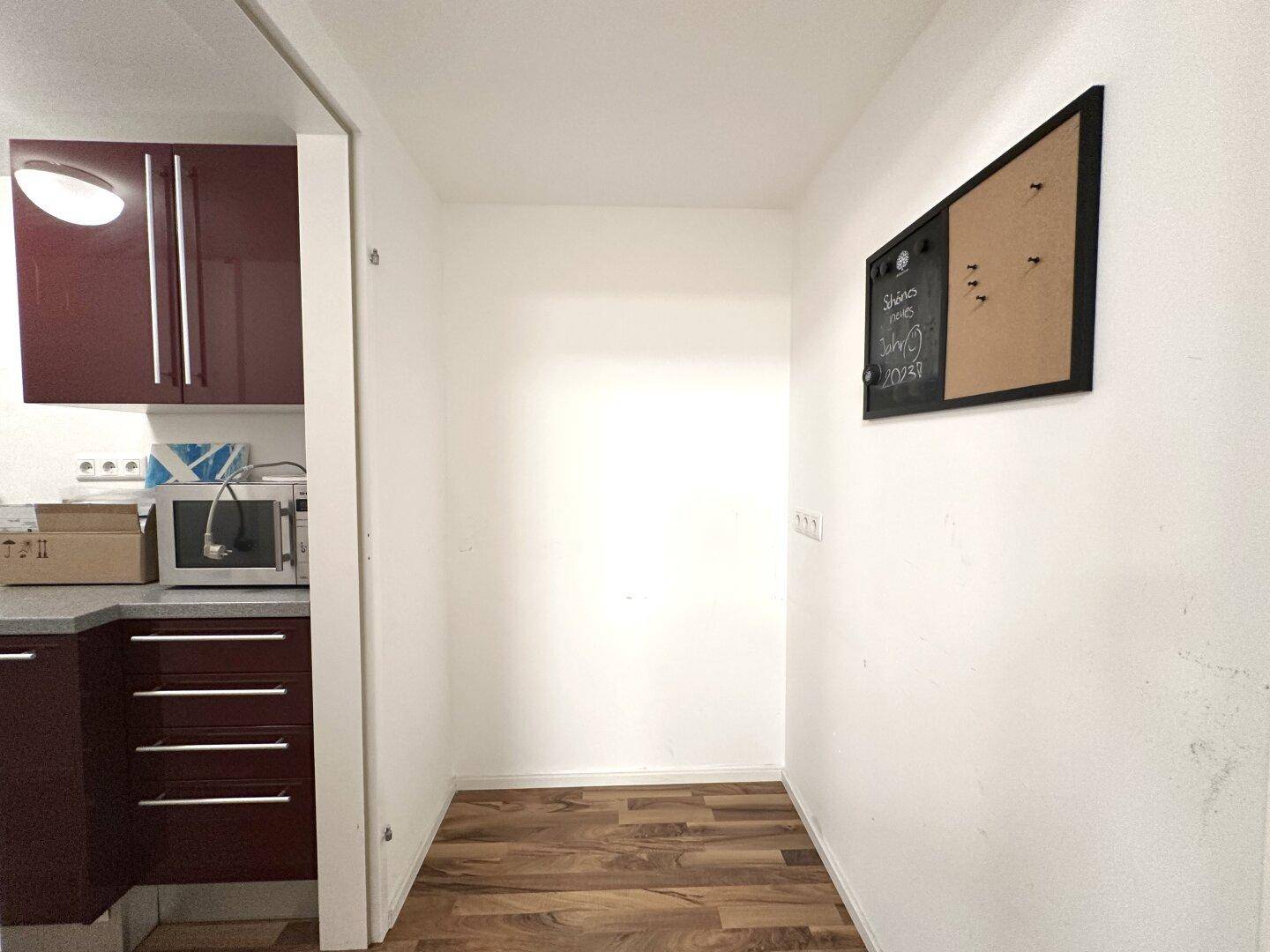 Kleiner Flur mit Holzboden und einer Pinnwand, der zu einer Küchenzeile führt.