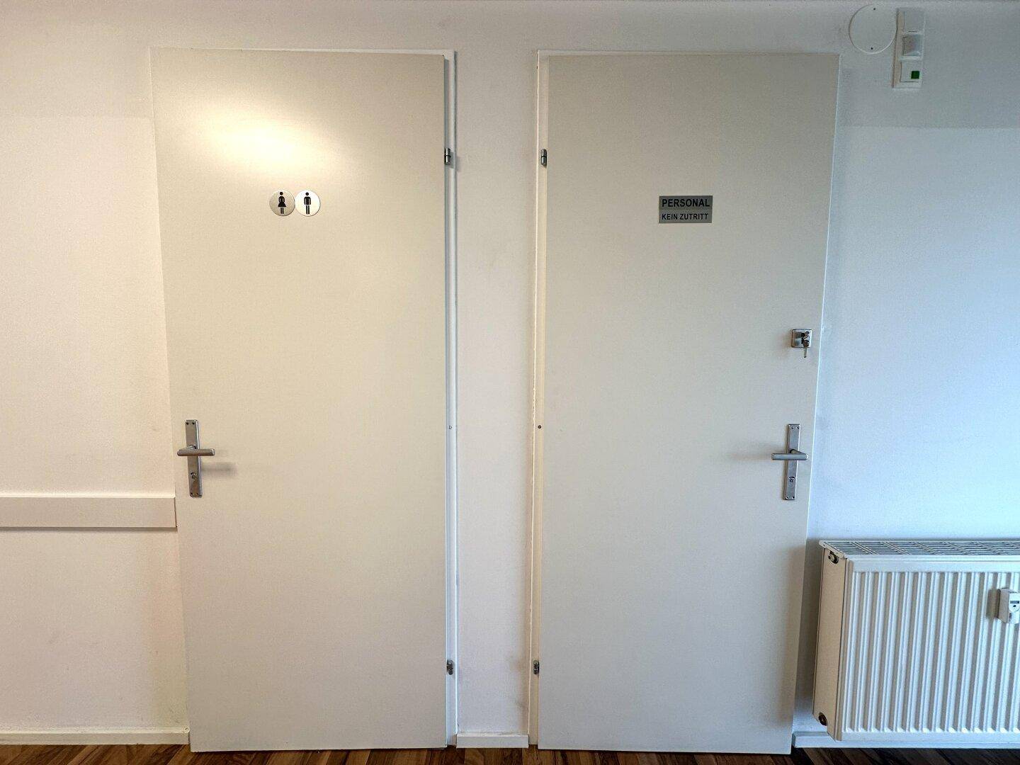 Zwei weiße Türen, eine für Toiletten und eine für Personal, mit Heizkörper darunter.