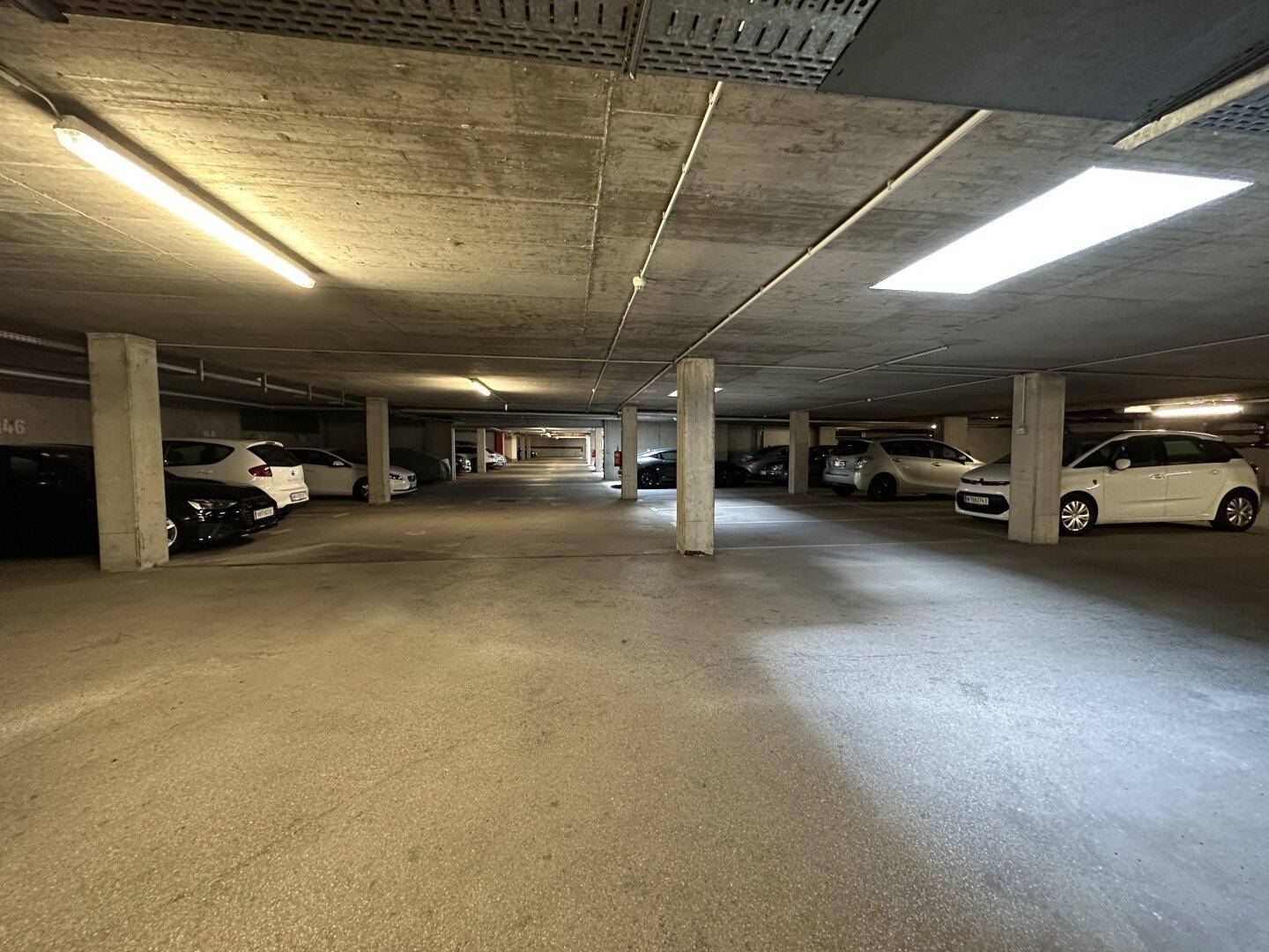 Tiefgarage mit zahlreichen geparkten Autos, Betonpfeilern und Deckenbeleuchtung.
