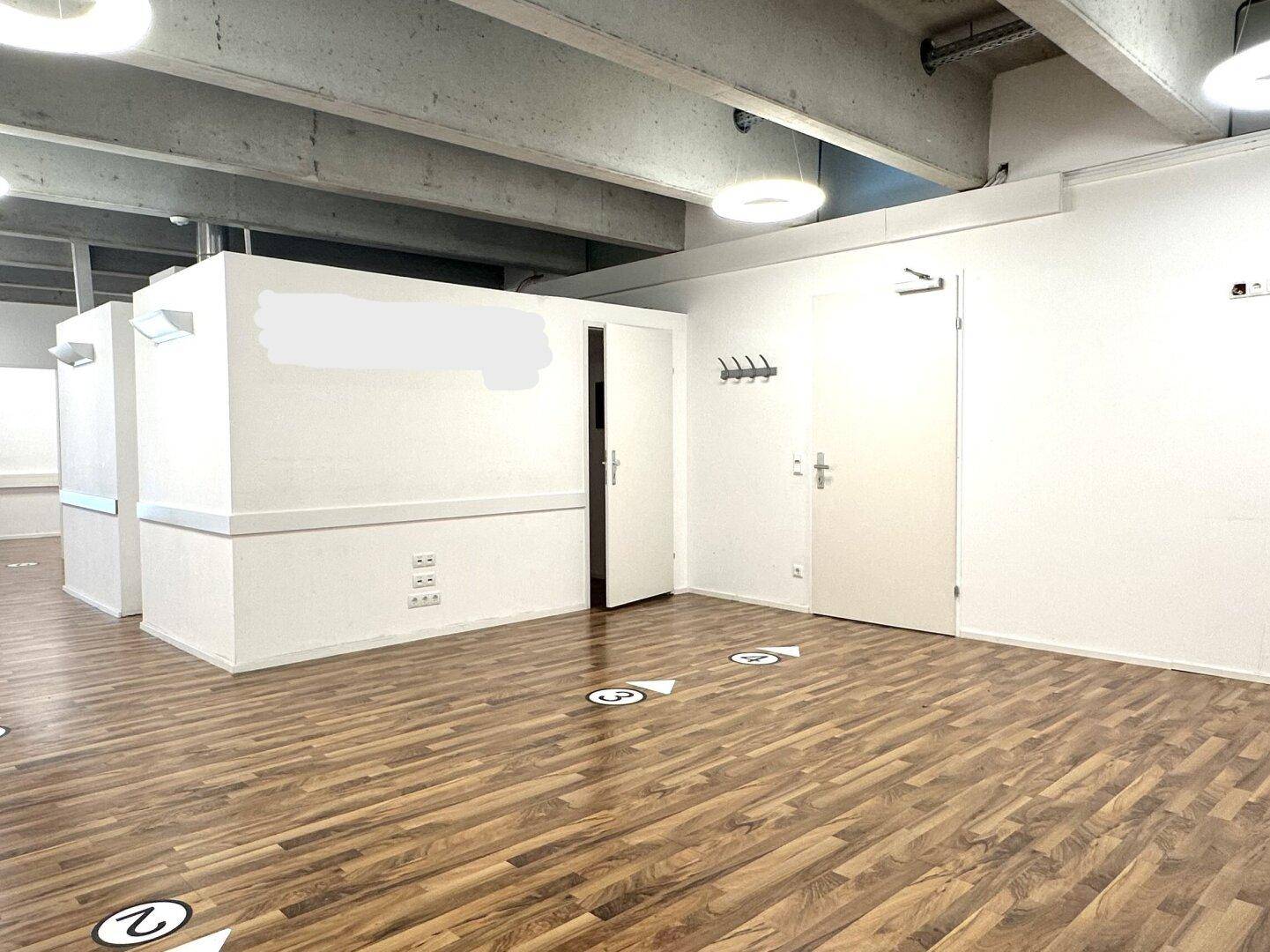 Großer offener Bürobereich mit Holzboden, Garderobe und modernen Deckenleuchten.