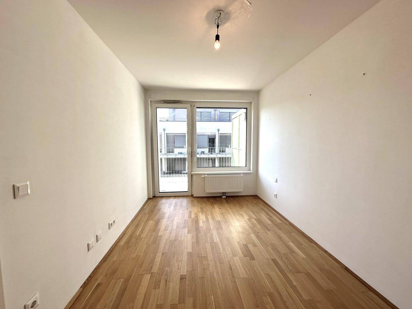 Geräumiger, heller Raum mit Parkettboden und großen Fenstern, die viel Tageslicht hereinlassen.