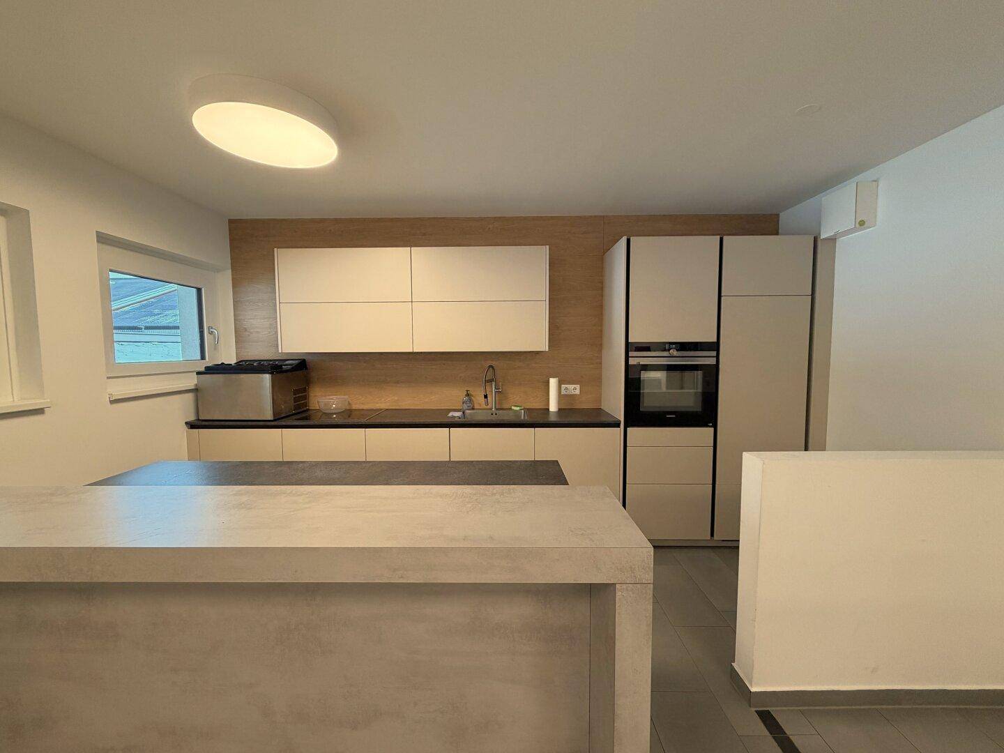 Moderne Küche mit Kücheninsel, hellen Schränken und Holzakzenten an der Wand.