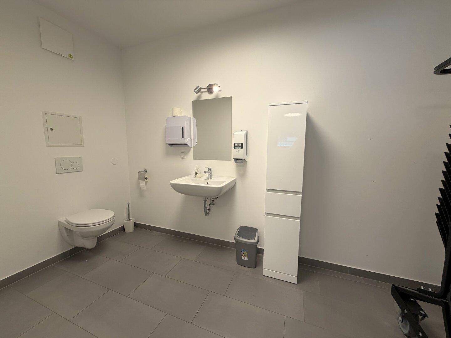 Helles WC mit wandhängender Toilette, Waschbecken und Fliesenboden.