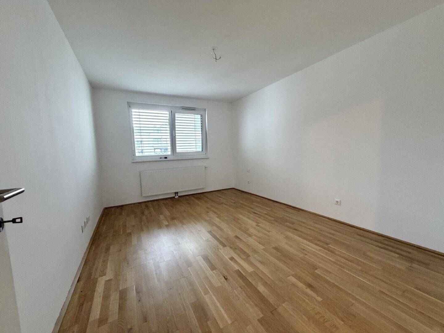 Geräumiges Schlafzimmer mit hellem Parkettboden und Fenster, ideal für Ruhe und Entspannung.
