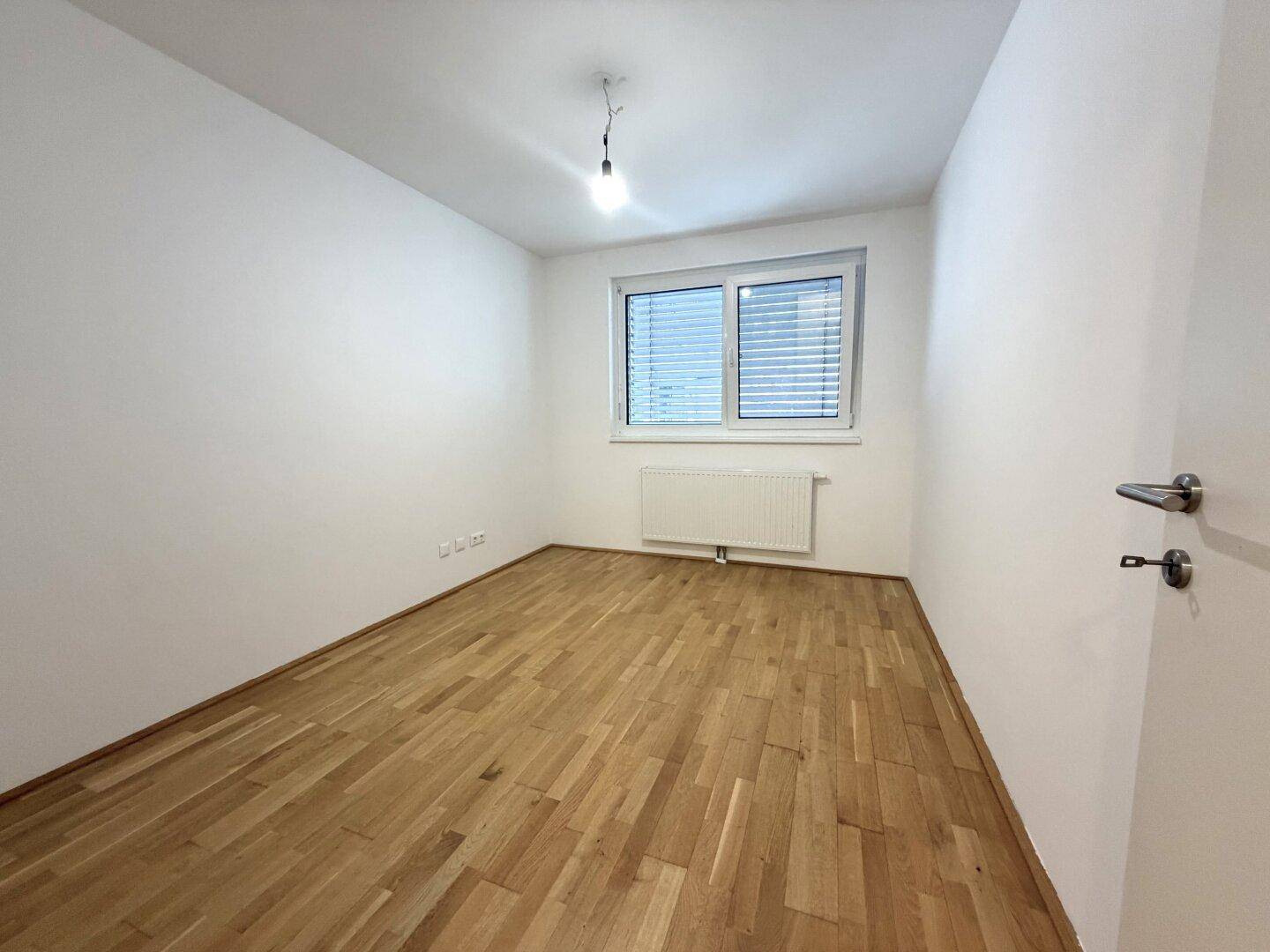 Helles Schlafzimmer mit Parkettboden und großem Fenster, bereit zur individuellen Gestaltung.