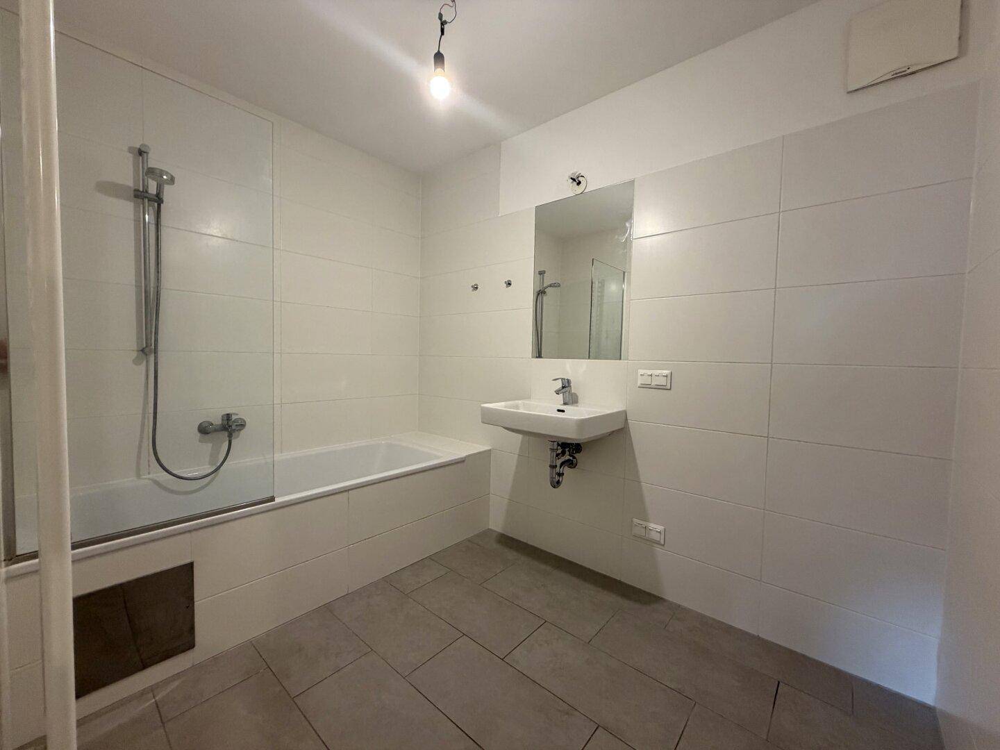 Modernes Badezimmer mit Badewanne, Dusche und weißen Fliesen.