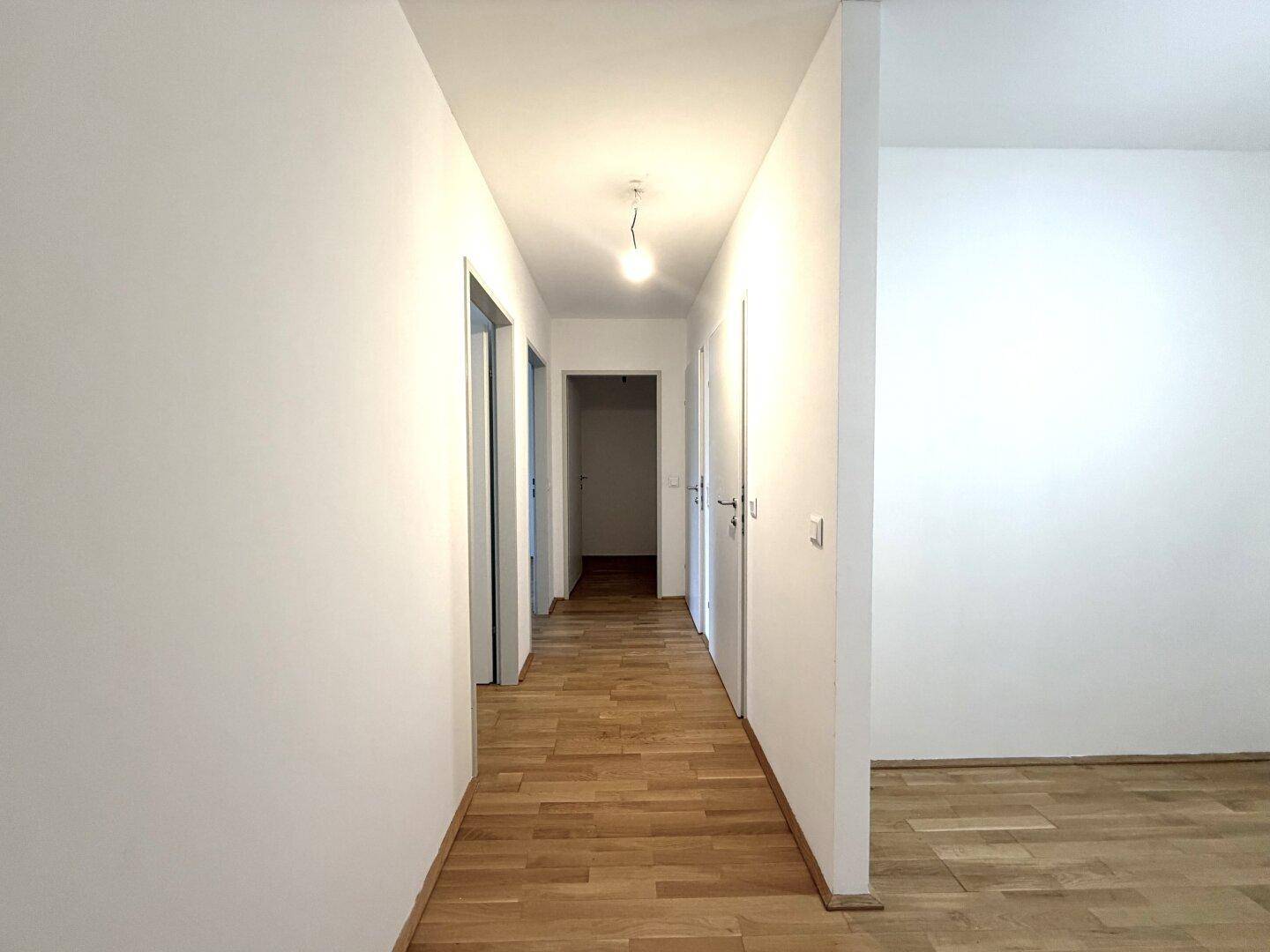 Langer, heller Flur mit Parkettboden, der verschiedene Zimmer miteinander verbindet.