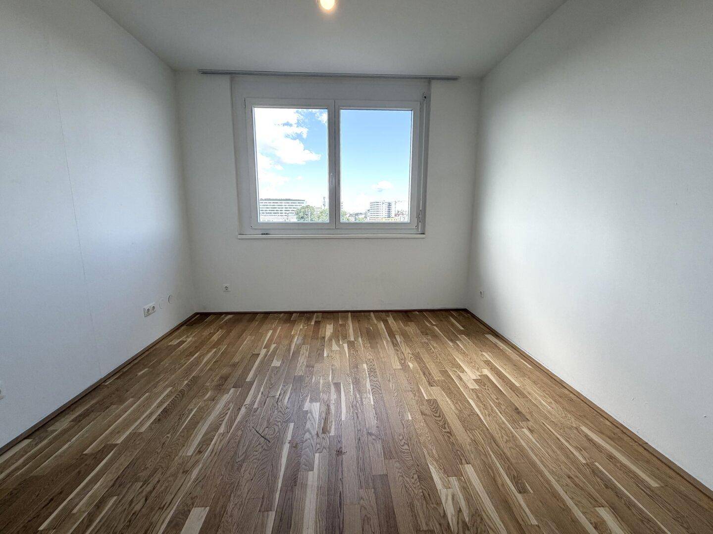 Helles Schlafzimmer mit Parkettboden und einem großen Fenster mit Stadtblick.